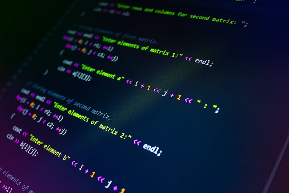 A close-up image of a person's hand operating a laptop computer placed on a wooden surface. The laptop screen displays lines of code in a text editor, suggesting programming or web development activit
